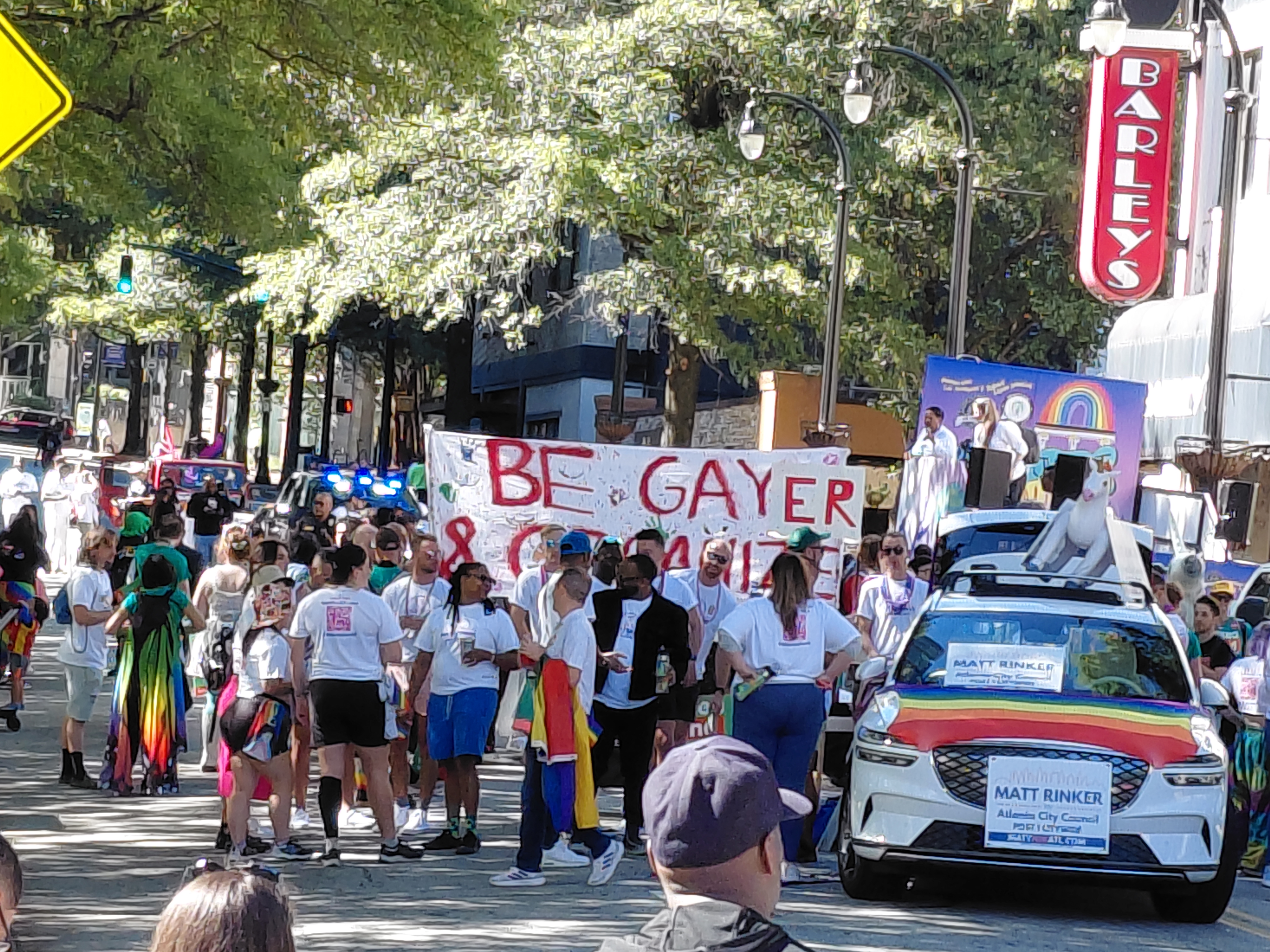 A picture from the setup for the Atlanta Pride Parade with a banner reading
"BE GAYER AND ORGANIZE" from the Kelsea Bond campaign. The "AND ORGANIZE" is
somewhat obscured by the crowd.